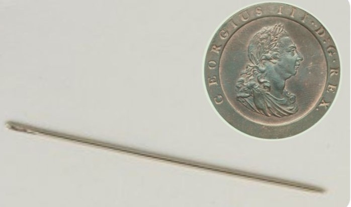 A steel sewing needle beside a George the third coin.